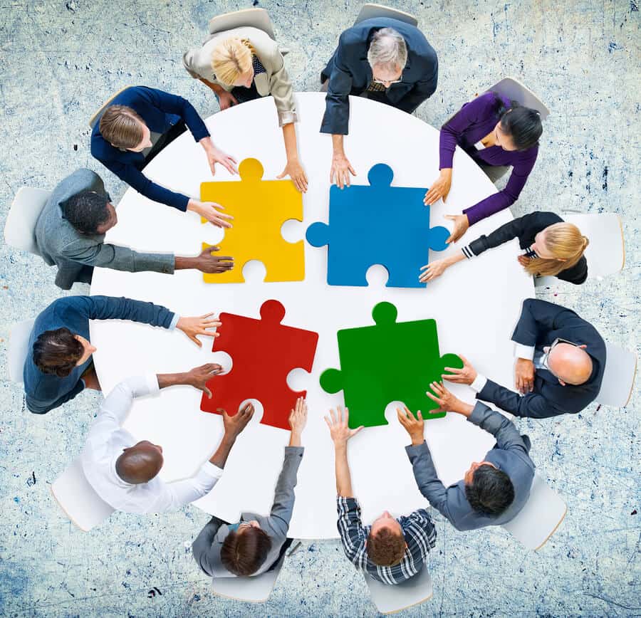 People around a round white table with a yellow, blue, red and green puzzle piecing them together