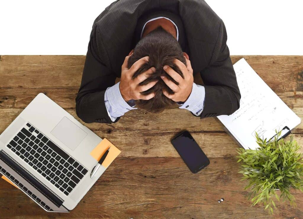 desperate stressed businessman sitting at office laptop computer desk with hands on his head crying devastated and frustrated in overwork and business crisis concept